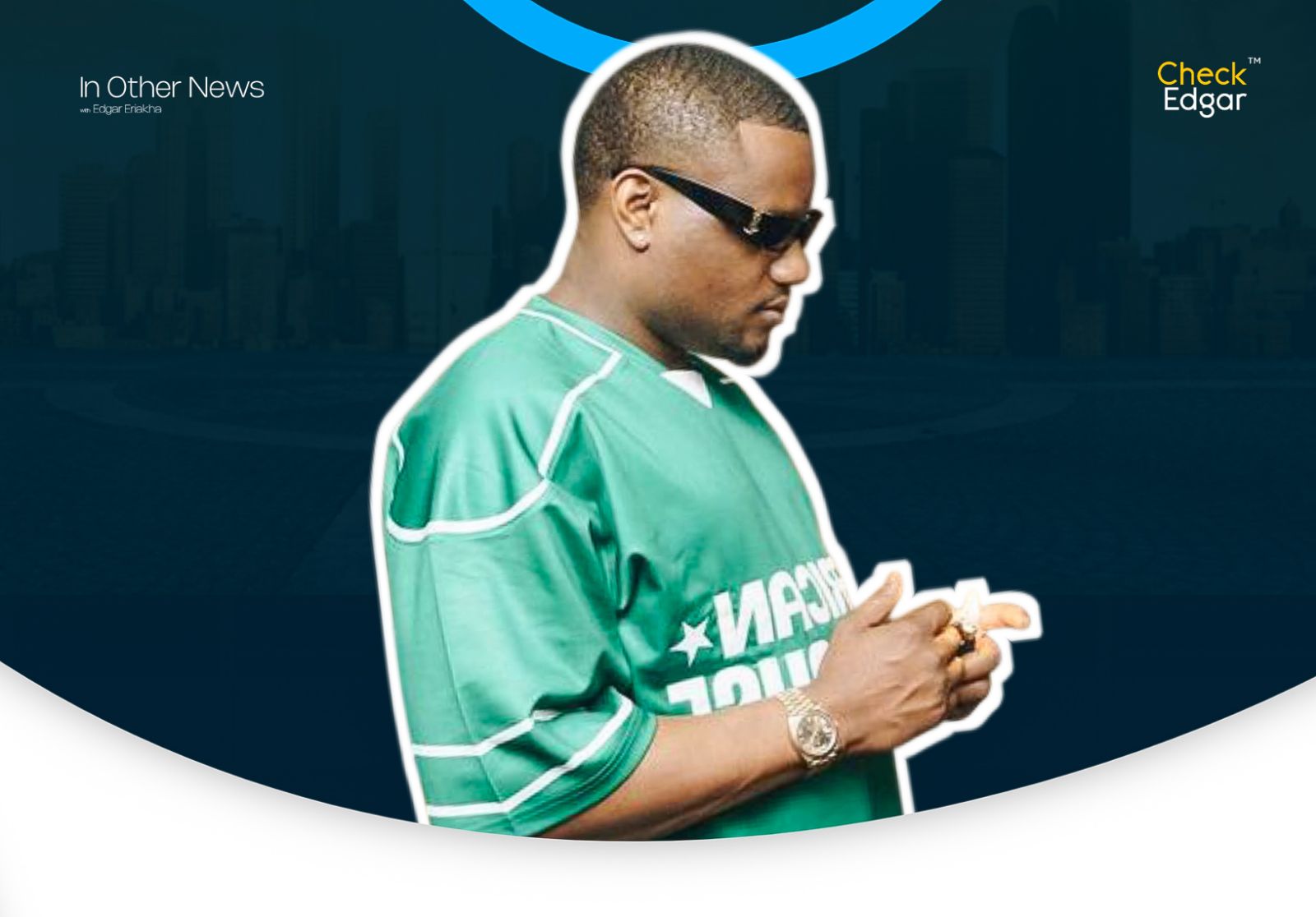 Dj Tunez in a green sports jersey looking down at his hands, wearing sunglasses and a watch.