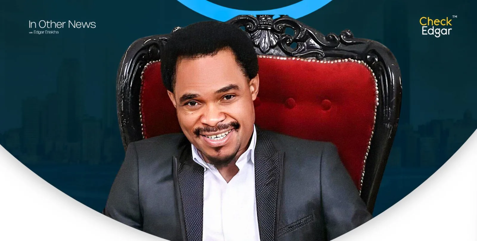 Odumeje in a black suit smiles while sitting on a red velvet chair.