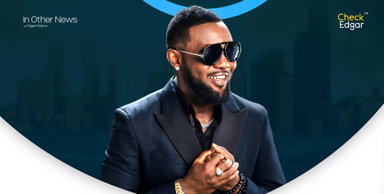 AY smiling with beard and sunglasses poses, wearing a black suit.