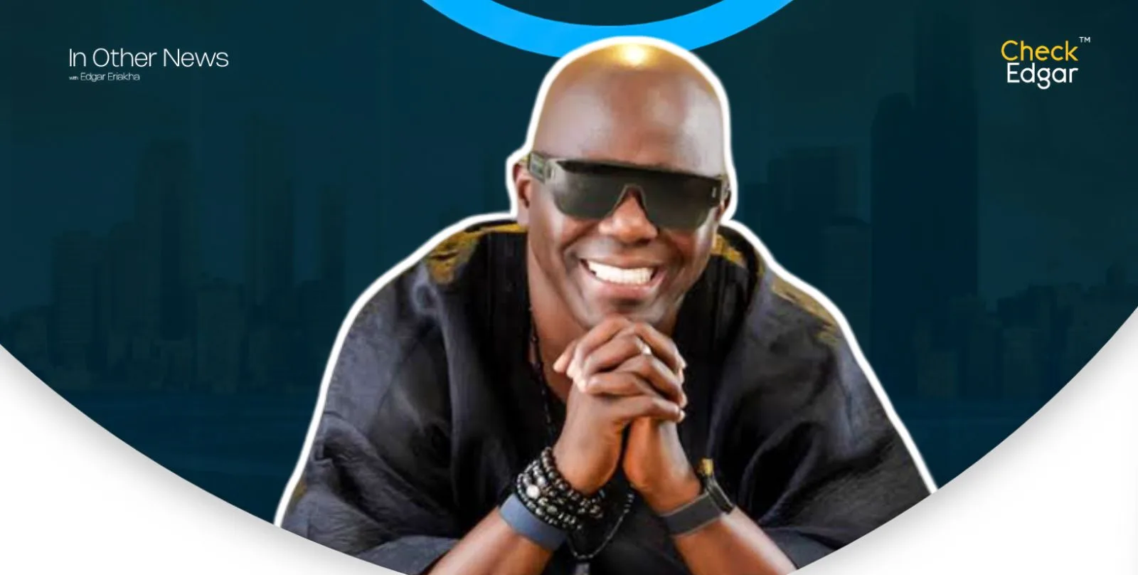 Ayo Animashaun in dark sunglasses smiles while clasping his hands, wearing a black outfit and bracelets.